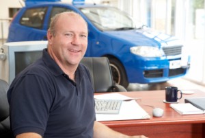 Car salesman sitting in showroom smiling